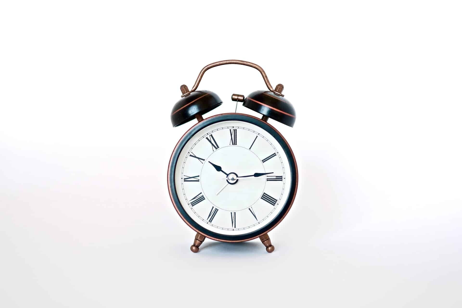 A classic round, black-and-white alarm clock with Roman numerals and two bells on top, set against a plain white background. The time displayed is 10:09, as we await news that the 2023 Income Limits Delayed have been resolved.