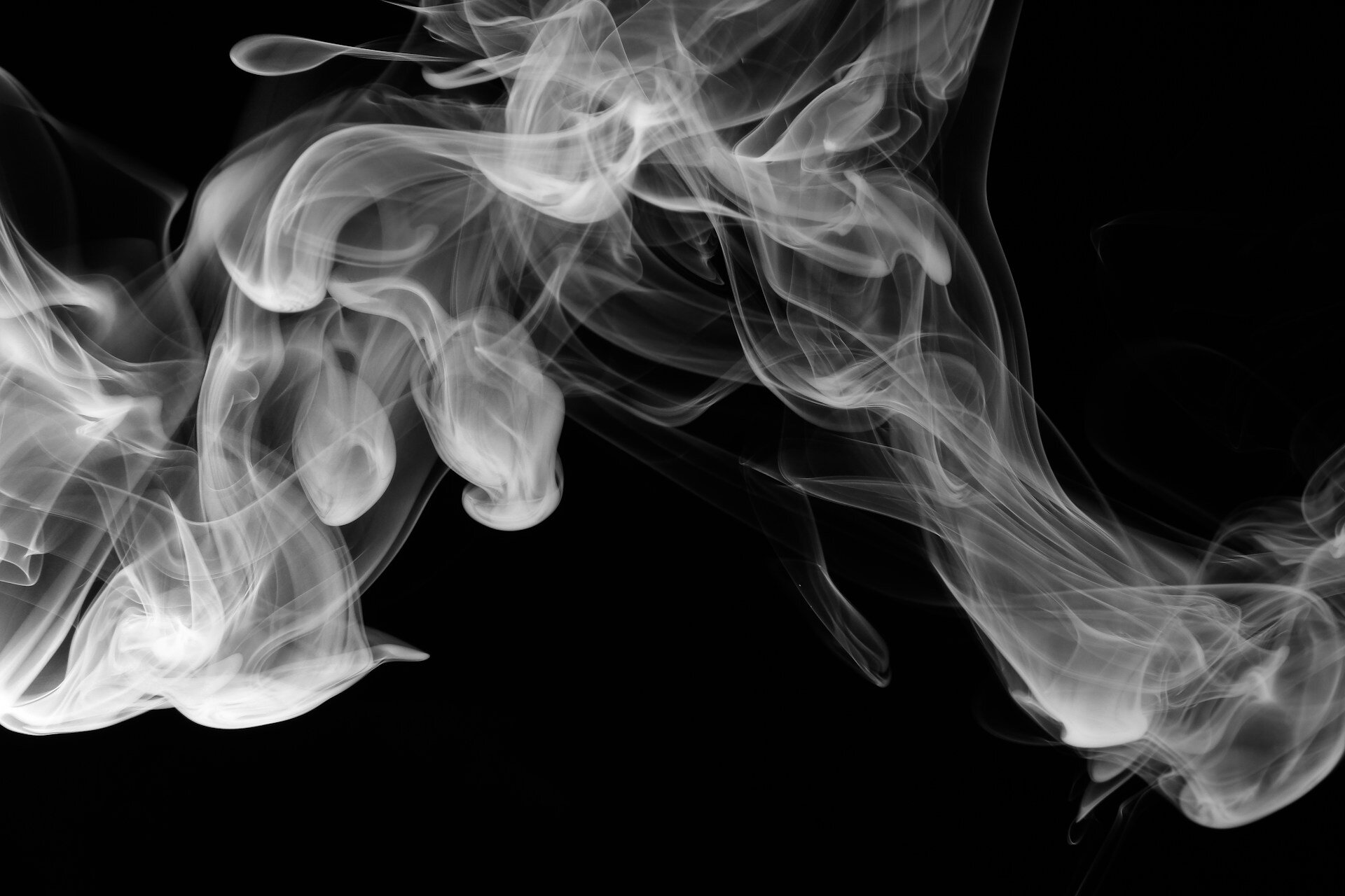 Wisps of white smoke swirl and curl against a black background, creating intricate, fluid patterns.